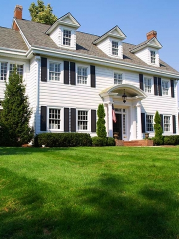 Two story traditional home with lots of green grass, American flag, two chimneys