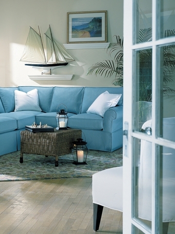 Entering a room with hardwood floors, blue sofa, chess board and boat sculpture on wall.